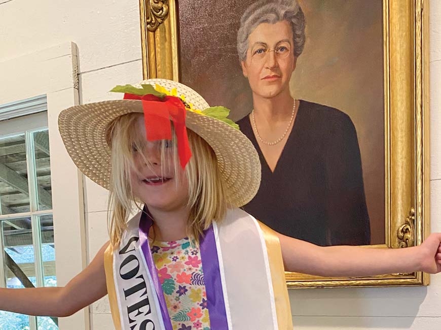 Petra Ann Austin, great-great-granddaughter of Gertrude Dills McKee, sports a suffragette sash in front a portrait of McKee displayed in the Cashiers Historical Society’s XIX Amendment Exhibit. Donated photo