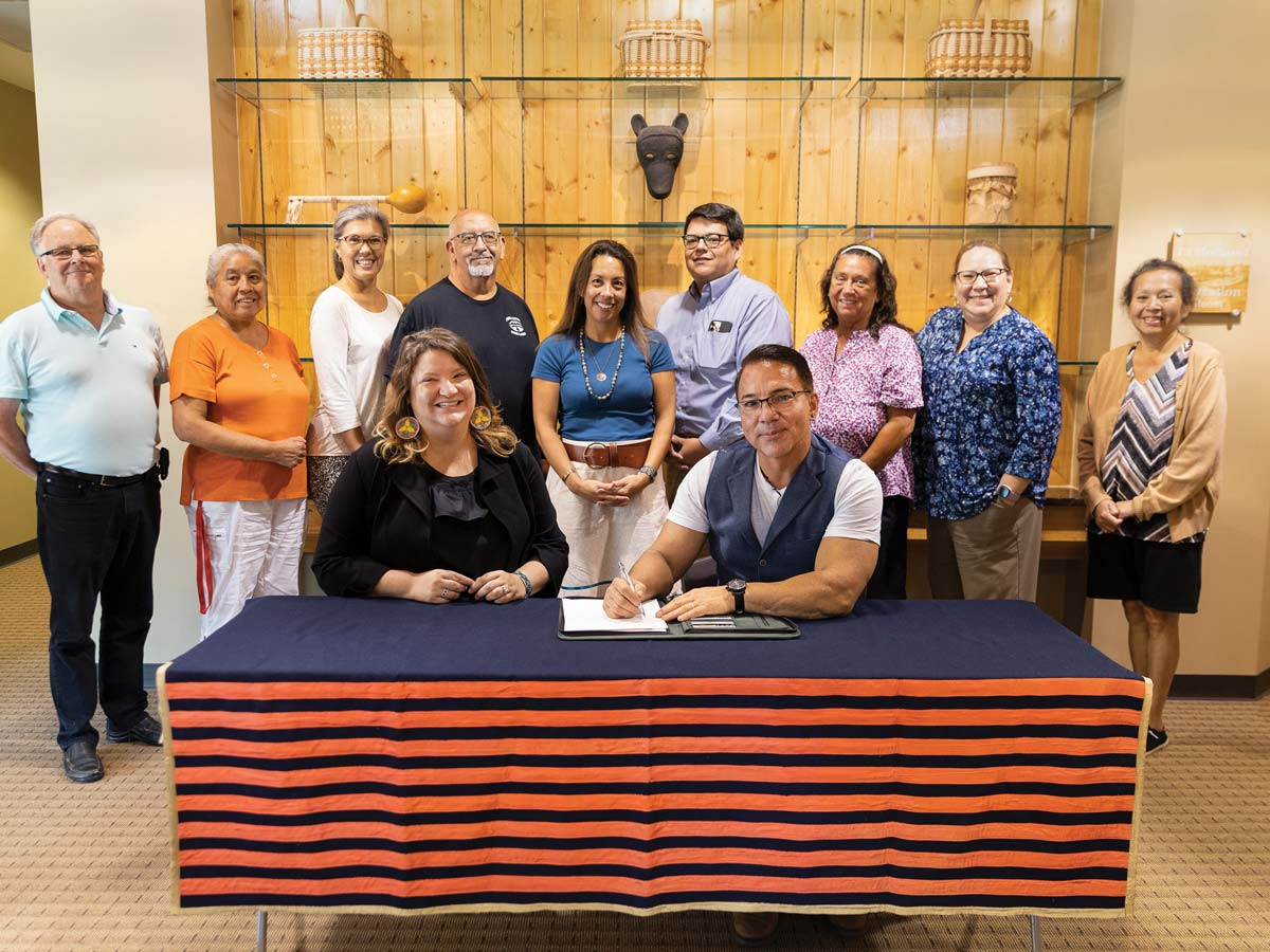 Principal Chief Richard G. Sneed (R) signs a land use permit recently allowing the Museum of the Cherokee Indian to operate an offsite facility housing Museum collections, archives, and Tribal artifacts on land in Swain County. Shown, left to right, back row — Lambert Wilson, Marie Junaluska, Anita Lossiah, Perry Shell, Shana Condill, Cory Blankenship, Myra Cloer, Dawna Paul, Louise Reed; seated Samantha Ferguson and Chief Sneed.                              Photo from The Museum of the Cherokee Indian