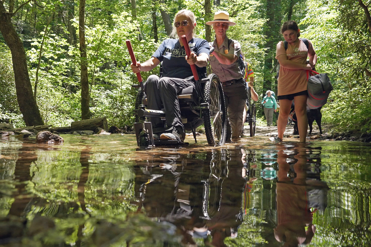 Park Ranger Katie Corrigan helps Carly Peterson, ADA coordinator for Knox County and volunteer for Catalyst Sports, navigate a creek crossing on Cooper Road Trail. Jim Matheny, Friends of the Smokies photo