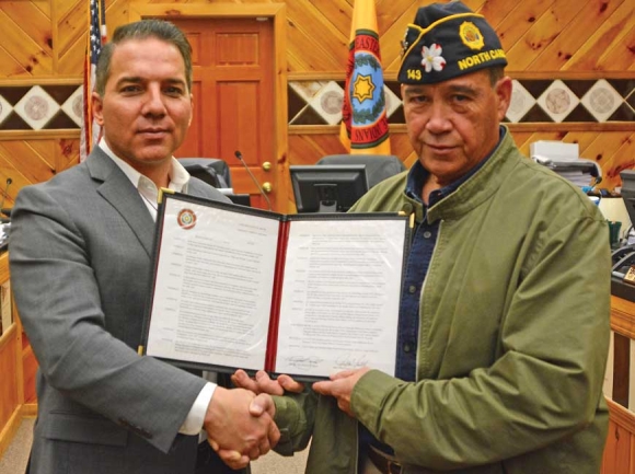 Kina Swayney’s husband Doug (right in right photo) shakes hands with Principal Chief Richard Sneed while holding the newly approved resolution honoring her as a Cherokee Beloved Woman. Holly Kays photo
