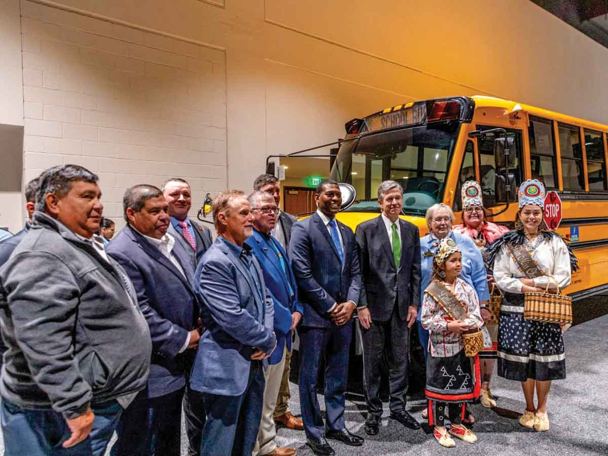 Tribal officials and representatives stand around the new school bus with N.C. Gov. Roy Cooper and EPA Administrator Michael Regan. EBCI Communications photo