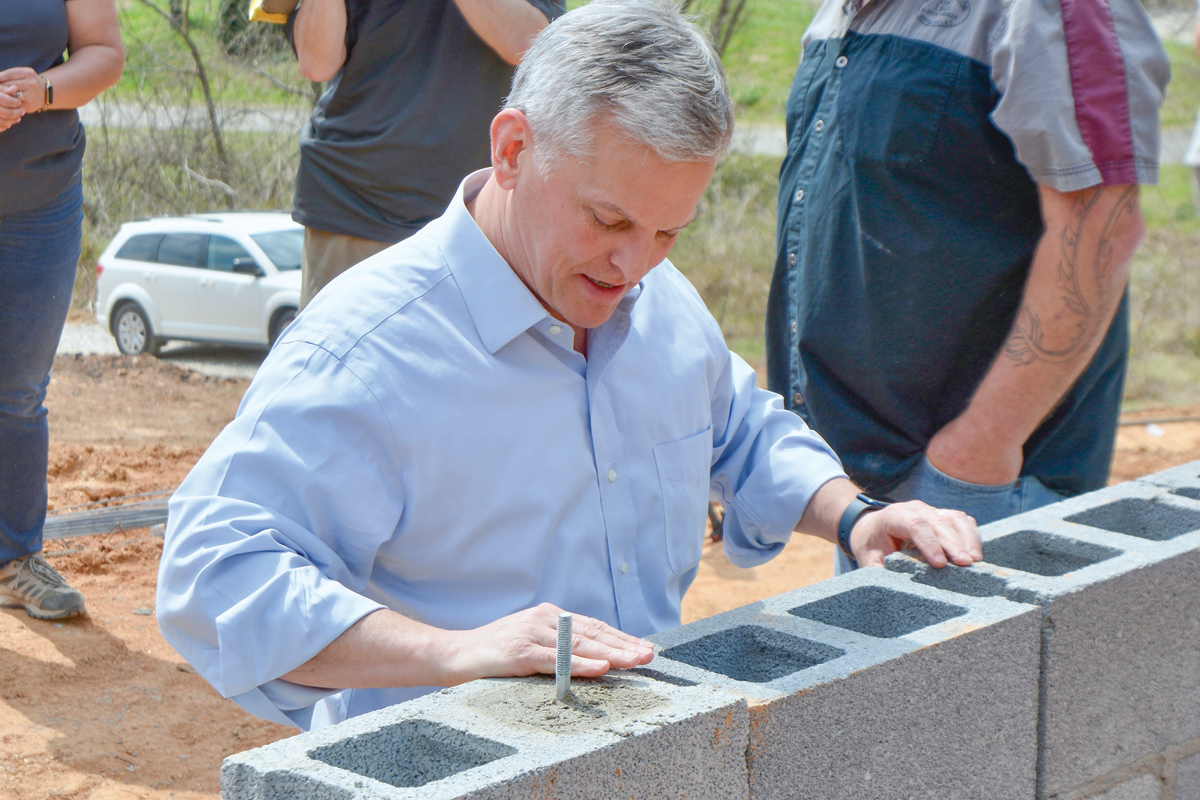 Gov. Josh Stein places a ceremonial block in the foundation of house under construction outside Bakersville. 