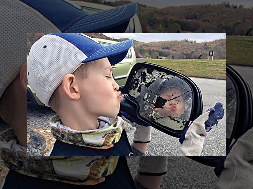 A young volunteer makes a face in a reflective piece of trash. Donated photo