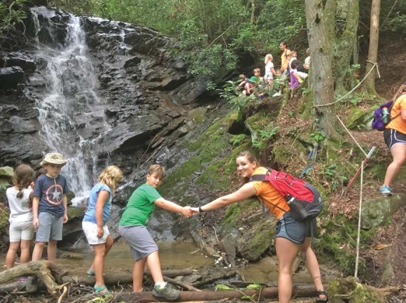 A camp counselor assists kids during a stream crossing. Donated photo