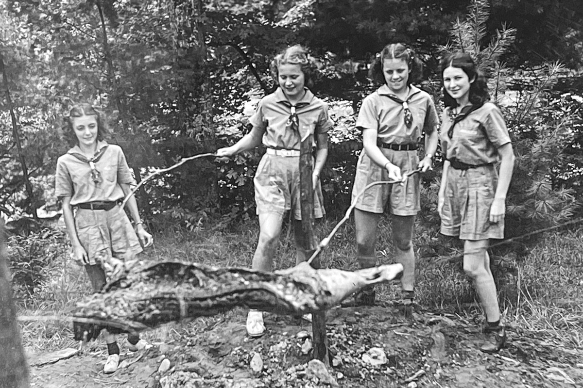 Elizabeth Hayes (left to right) Dot Hill, Edythe Mae Kincaid and Ann Rita Walland roast their dinner meal during a camp session in the 1930s. 